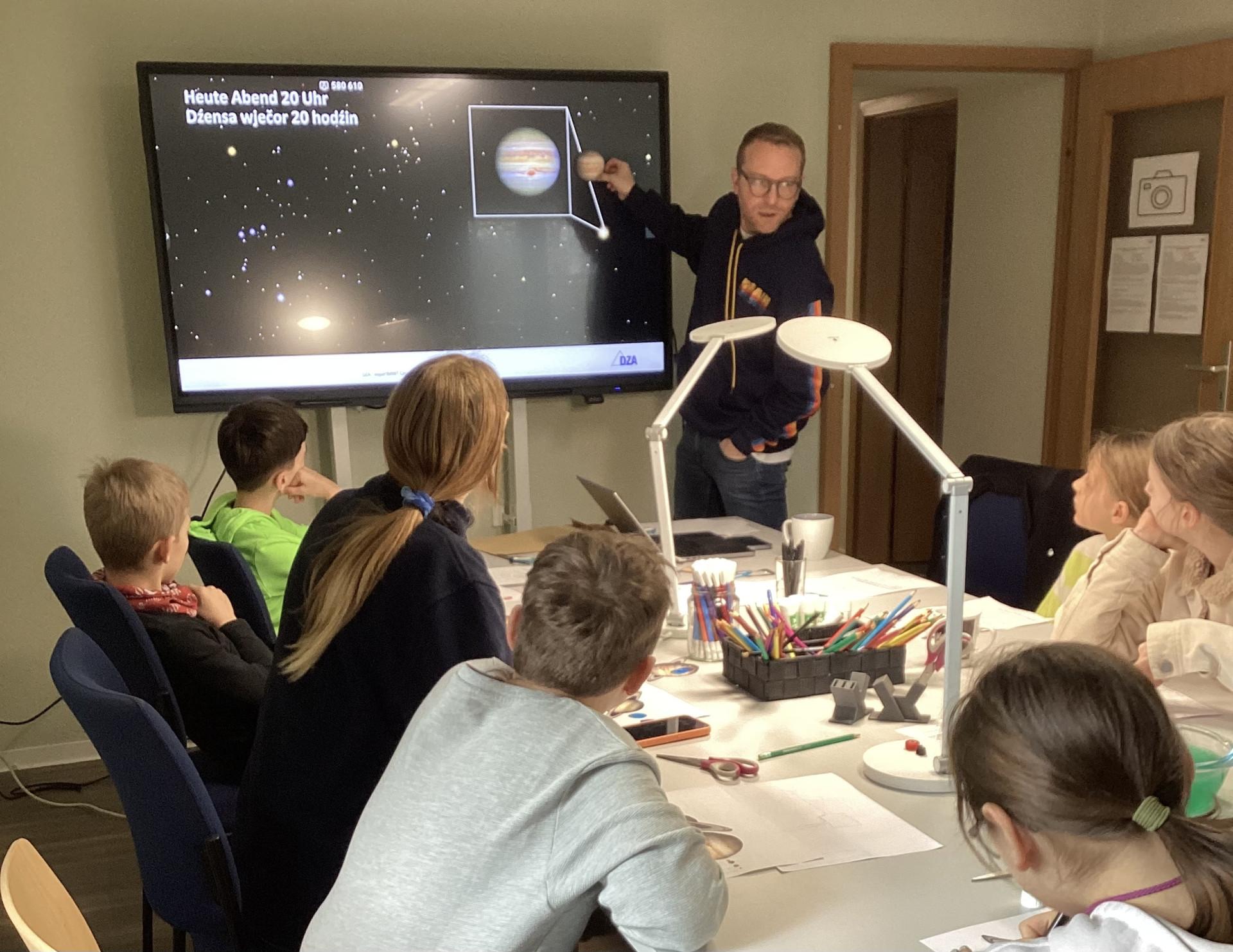 experi-MINT-Campus Radibor mit Dr. Stefan Ohm eine Gruppe von Schülern sitzt um einen Tisch und hören einem Mann mit Brille zu