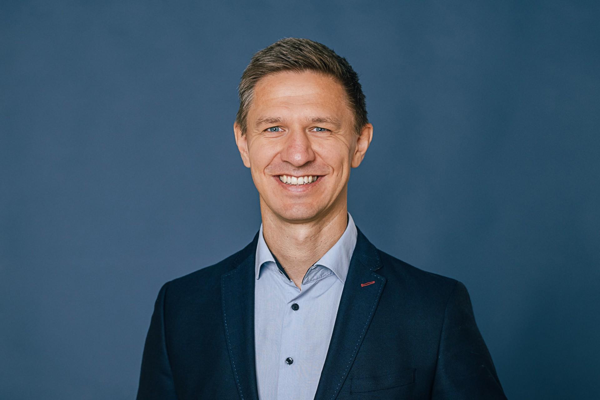 Mann mit kurzen Haaren, blauem Hemd und dunklem Sakko lächelt in die Kamera