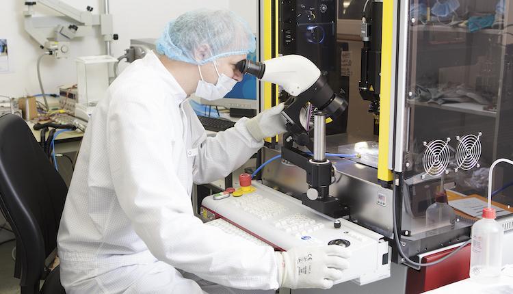 Researcher looks through microscope in clean room